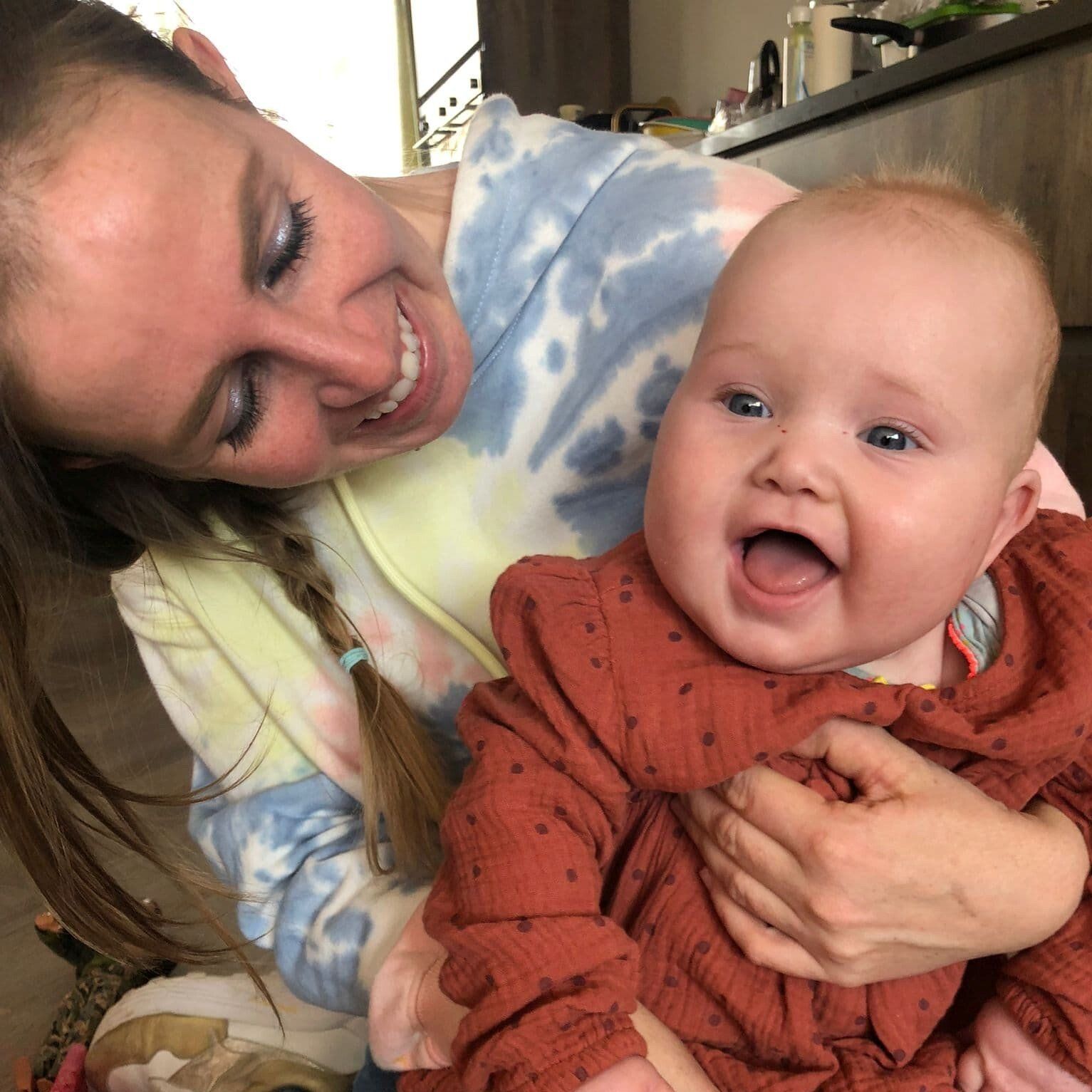 Een vrouw lacht en houdt een lachende baby vast in een gezellige binnenruimte.