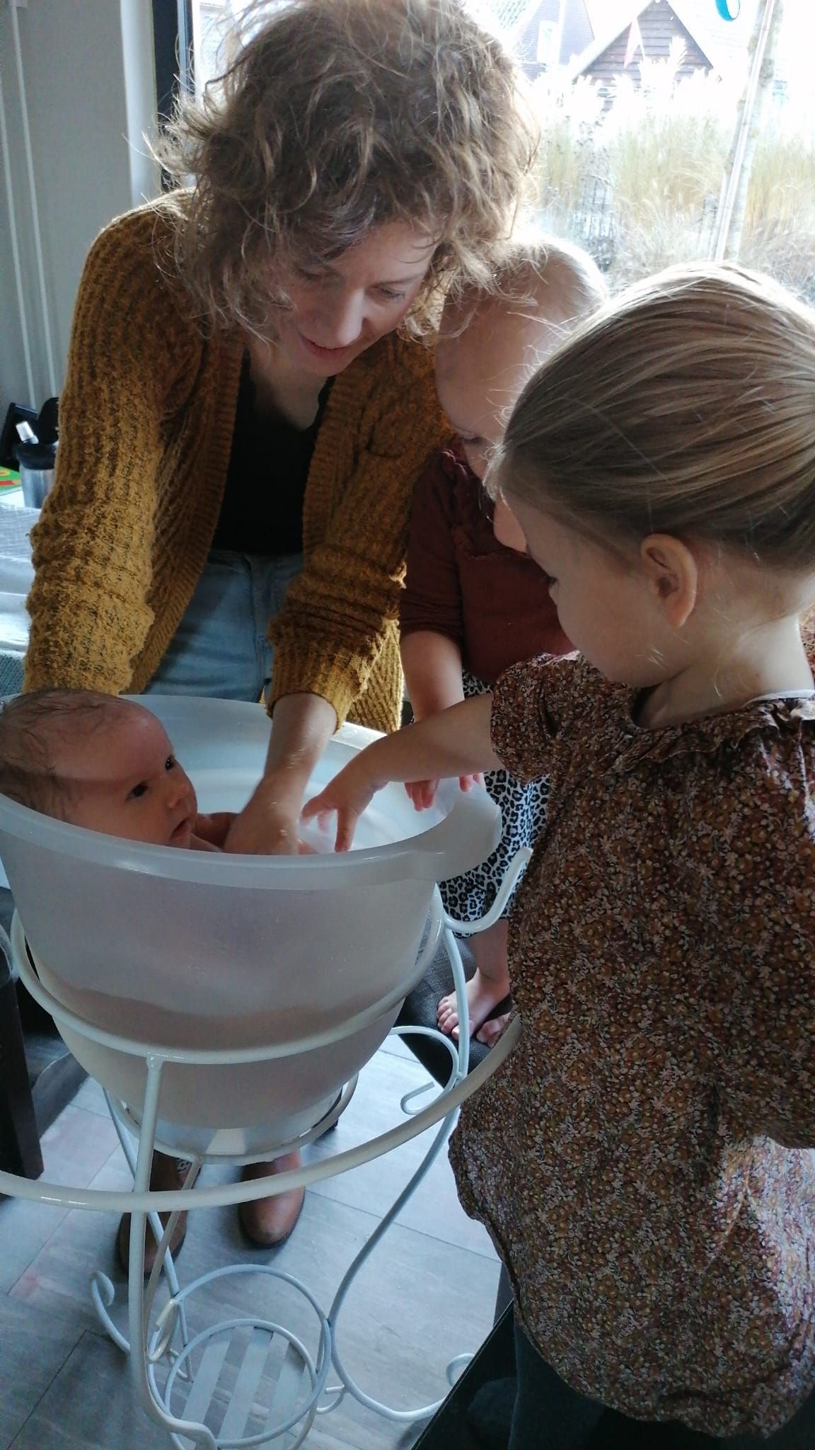 Een postpartumdoula helpt bij het in bad doen van een pasgeboren baby, samen met twee zusjes.