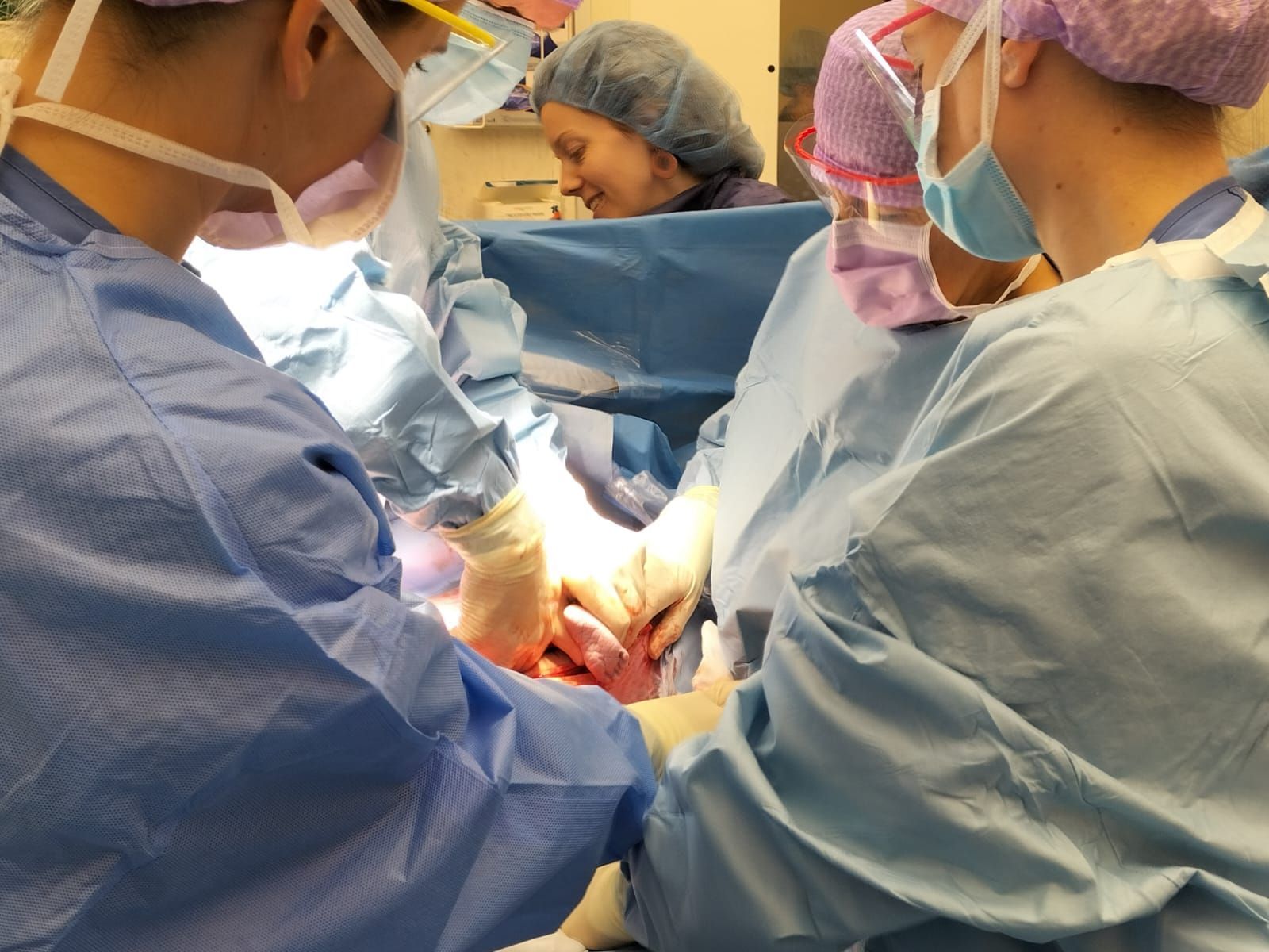 Medisch team in blauwe operatiekleding voert een operatie uit onder fel operatielicht.