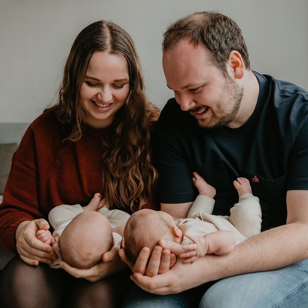 Een stel glimlacht naar twee slapende baby's die ze binnen in hun armen wiegen.