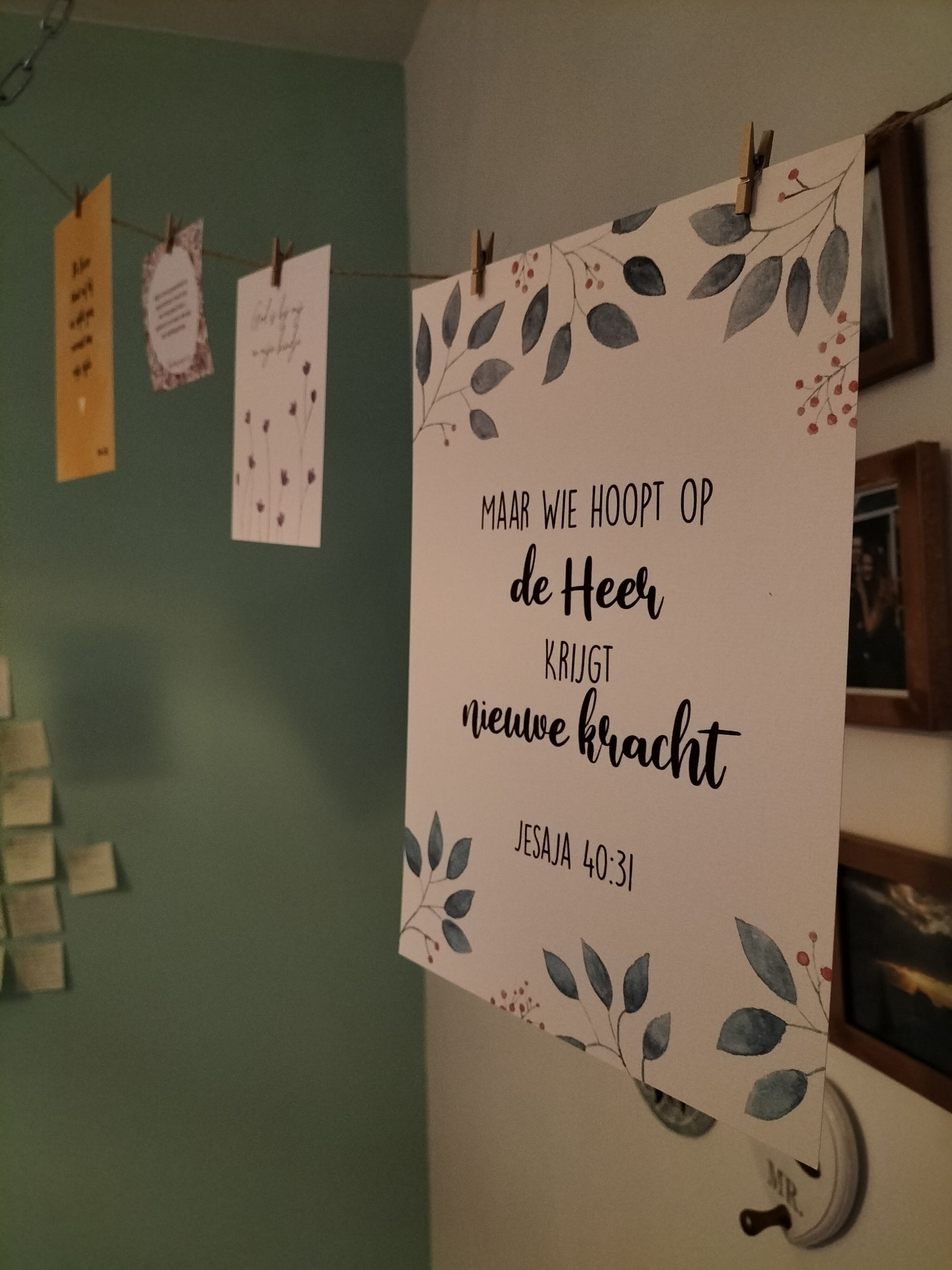 Wanddecoratie met hangende notitiekaartjes en een groot bord met een bloemmotief en een inspirerende quote op een groene muur.
