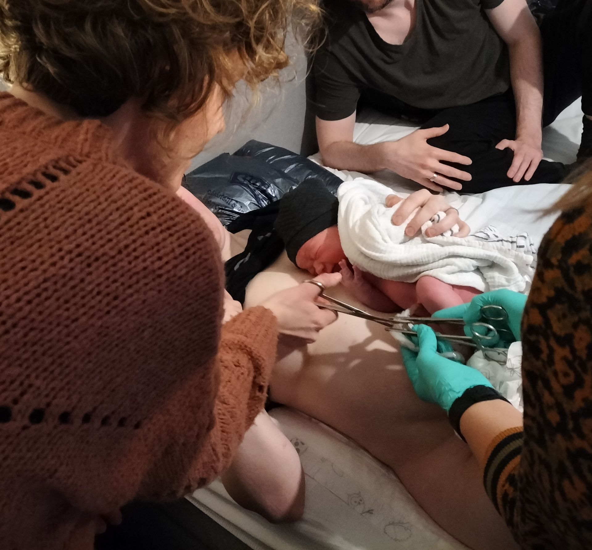 Een hand houdt een bord vast met beschuit met muisjes, naast twee brandende kaarsen op een vloer met warme tinten.