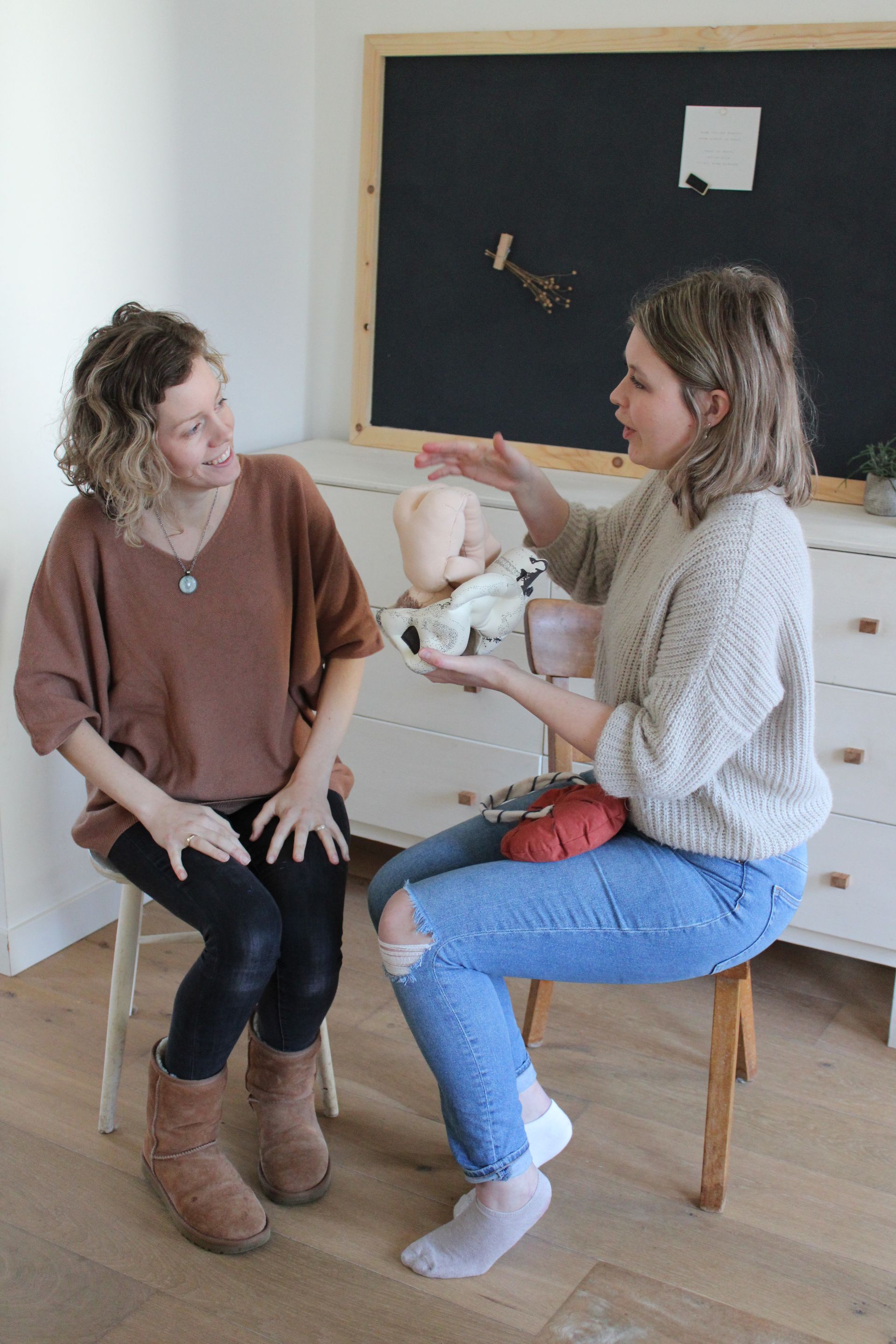 Twee vrouwen zitten in een kamer te praten, terwijl een van hen gebaren maakt tijdens het gesprek.