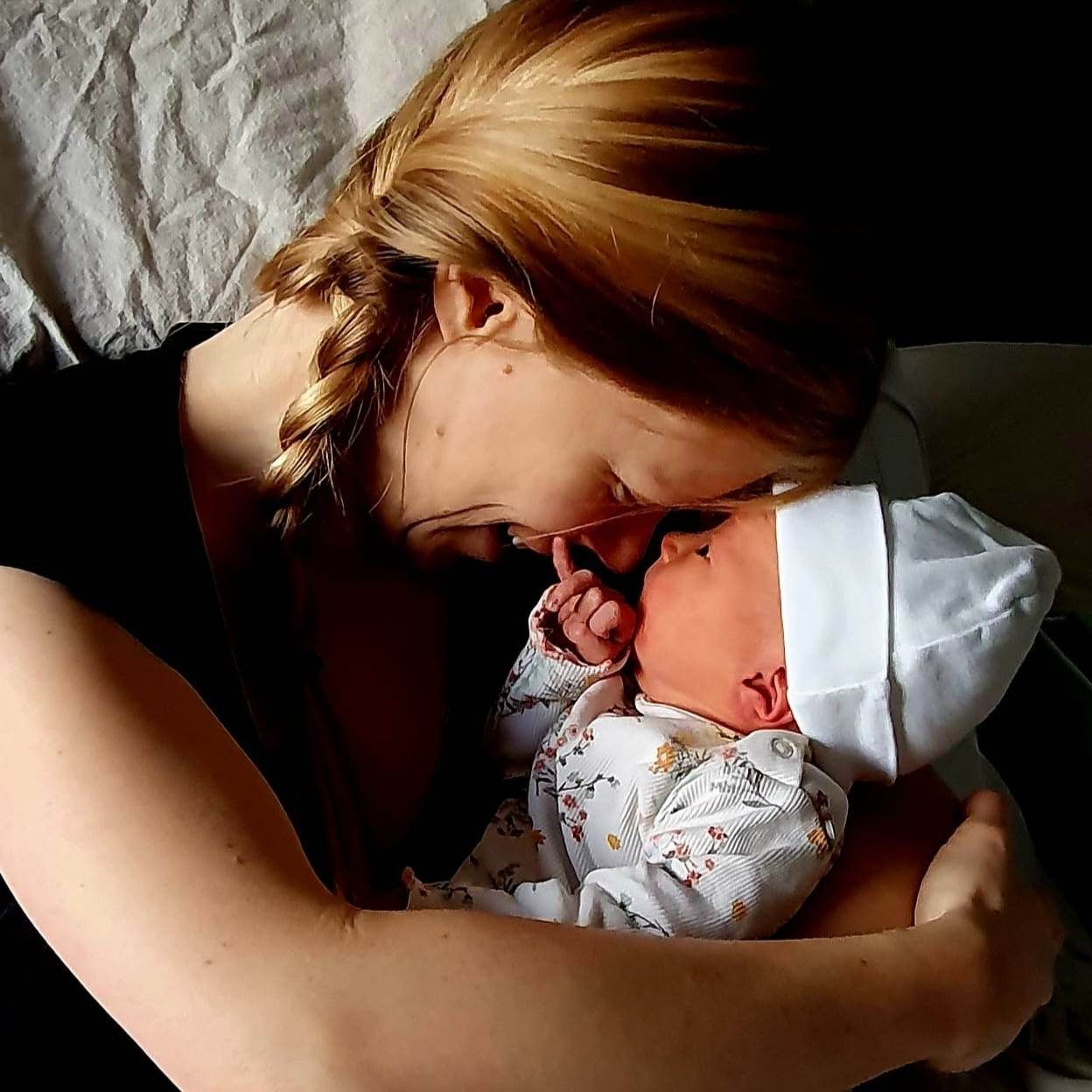 Een vrouw wiegt teder een slapende pasgeborene in een wit mutsje, hun gezichten raken elkaar in een teder, intiem moment.