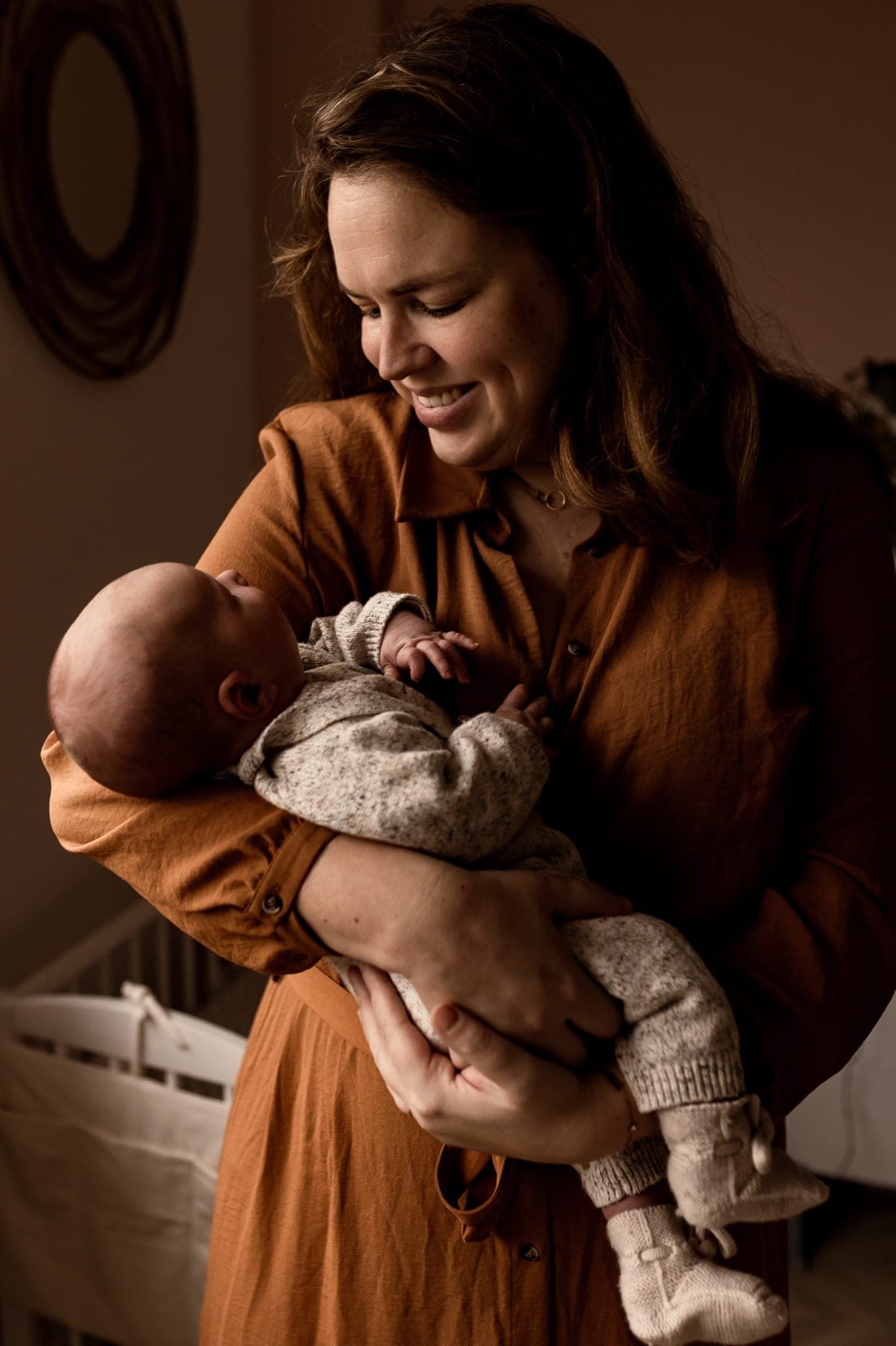 Vrouw houdt een slapende baby vast en lacht ernaar in een gezellige binnenkamer.