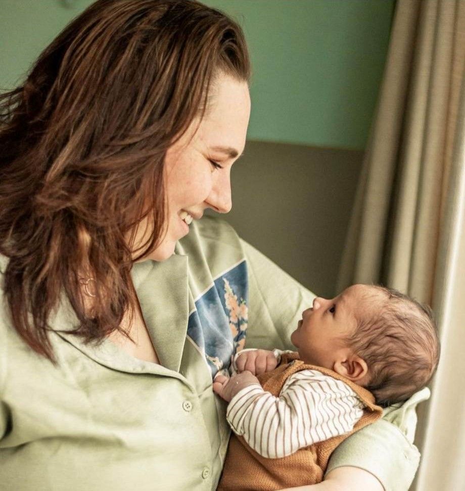 Een persoon glimlacht naar een baby in een ziekenkamer en houdt het kindje dicht tegen zich aan.