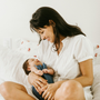 Vrouw lacht terwijl ze een baby vasthoudt in een helderwitte slaapkamer.
