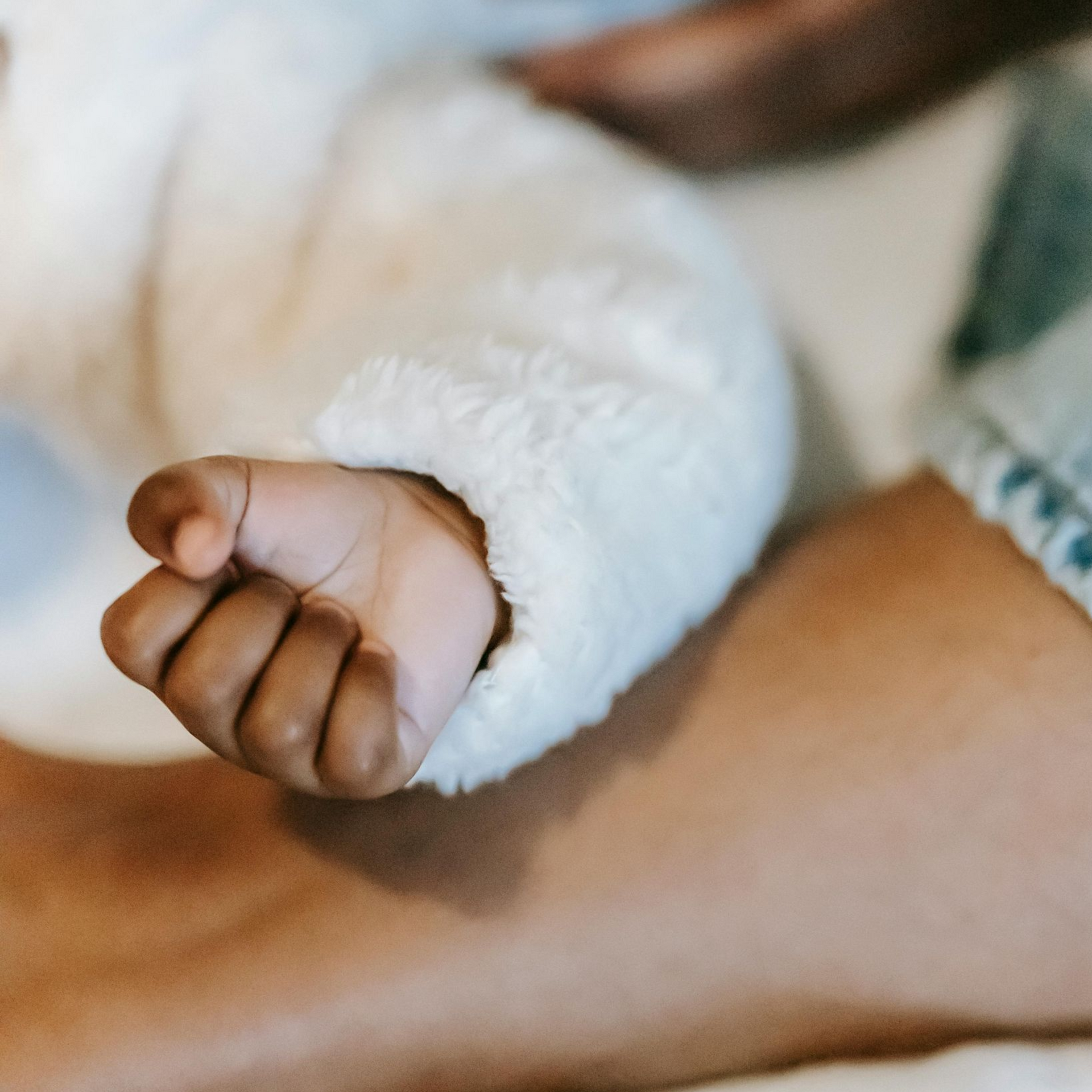 Een klein babyhandje rust op de arm van een volwassene, gewikkeld in een witte, pluizige hoes.