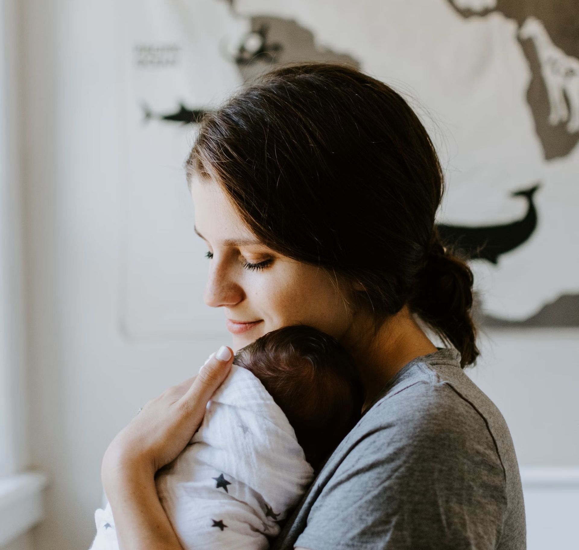 Vrouw houdt een slapende baby voorzichtig vast in een lichte kinderkamer.