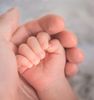 Een pasgeboren babyhandje houdt zachtjes de vinger van een volwassene vast, in een zachte close-up.