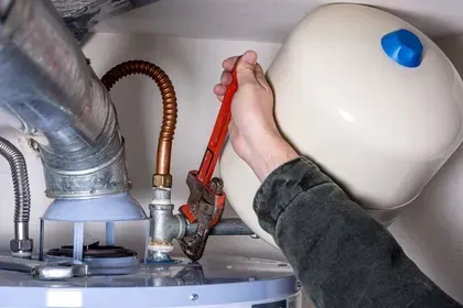 Plumber using a wrench to work on water heater in a utility room.