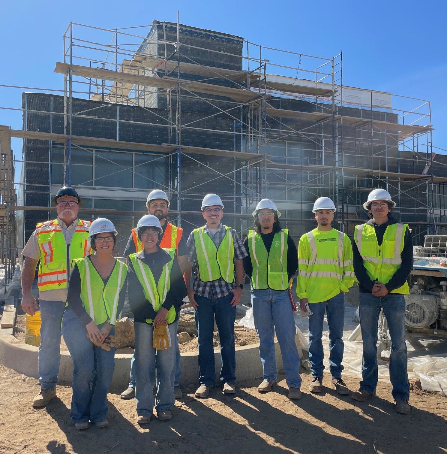 A group of people stand in front of a construction site in full PPE gear
