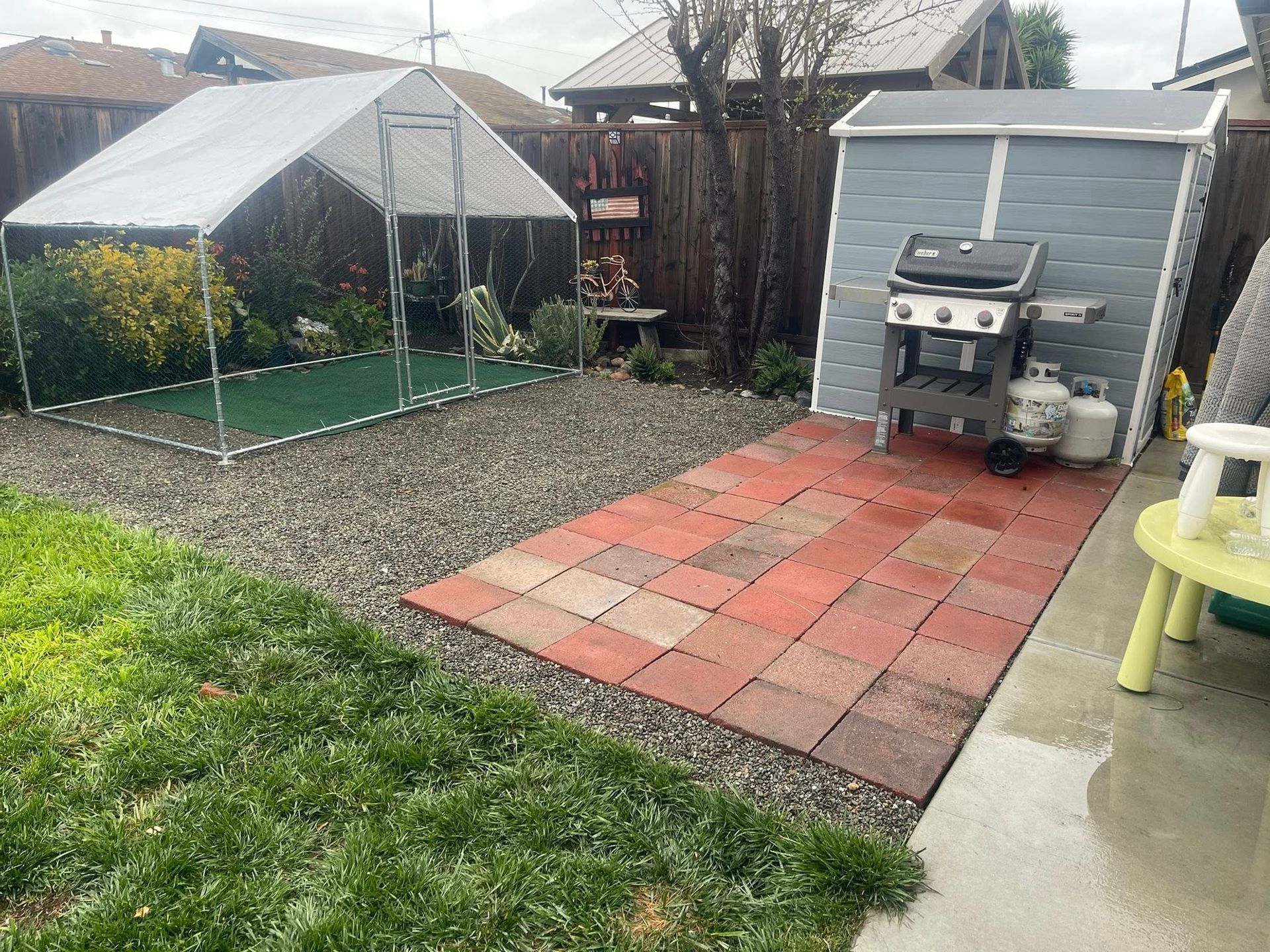 Backyard patio with pavers, gravel, greenhouse, shed, grill, and lawn.