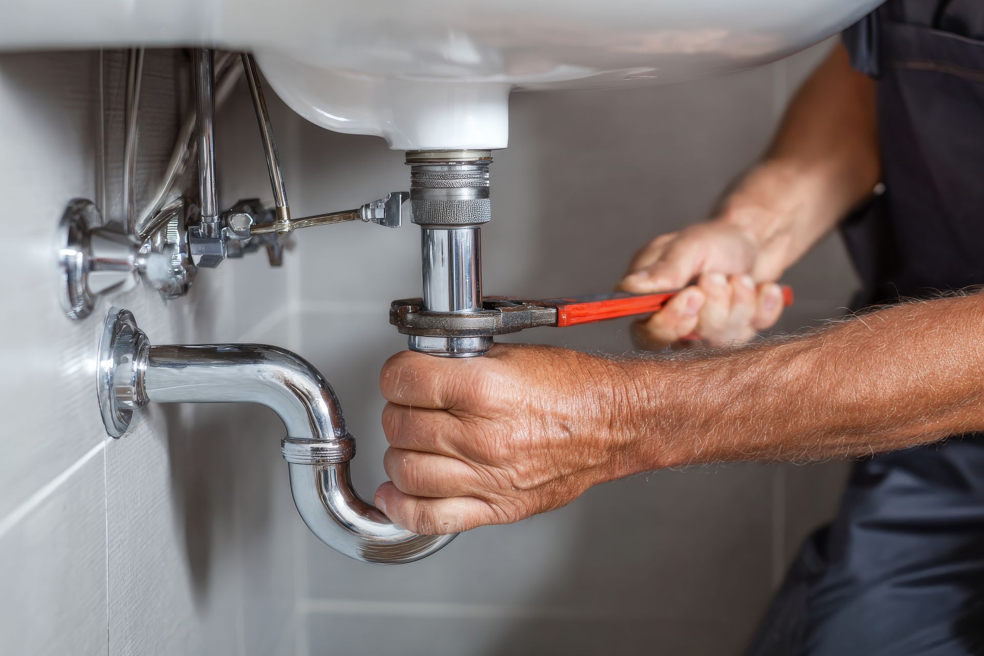 Plumber repairs sink plumbing with a wrench in a modern bathroom. Plumber repairs sink plumbing with a wrench in a modern bathroom.
