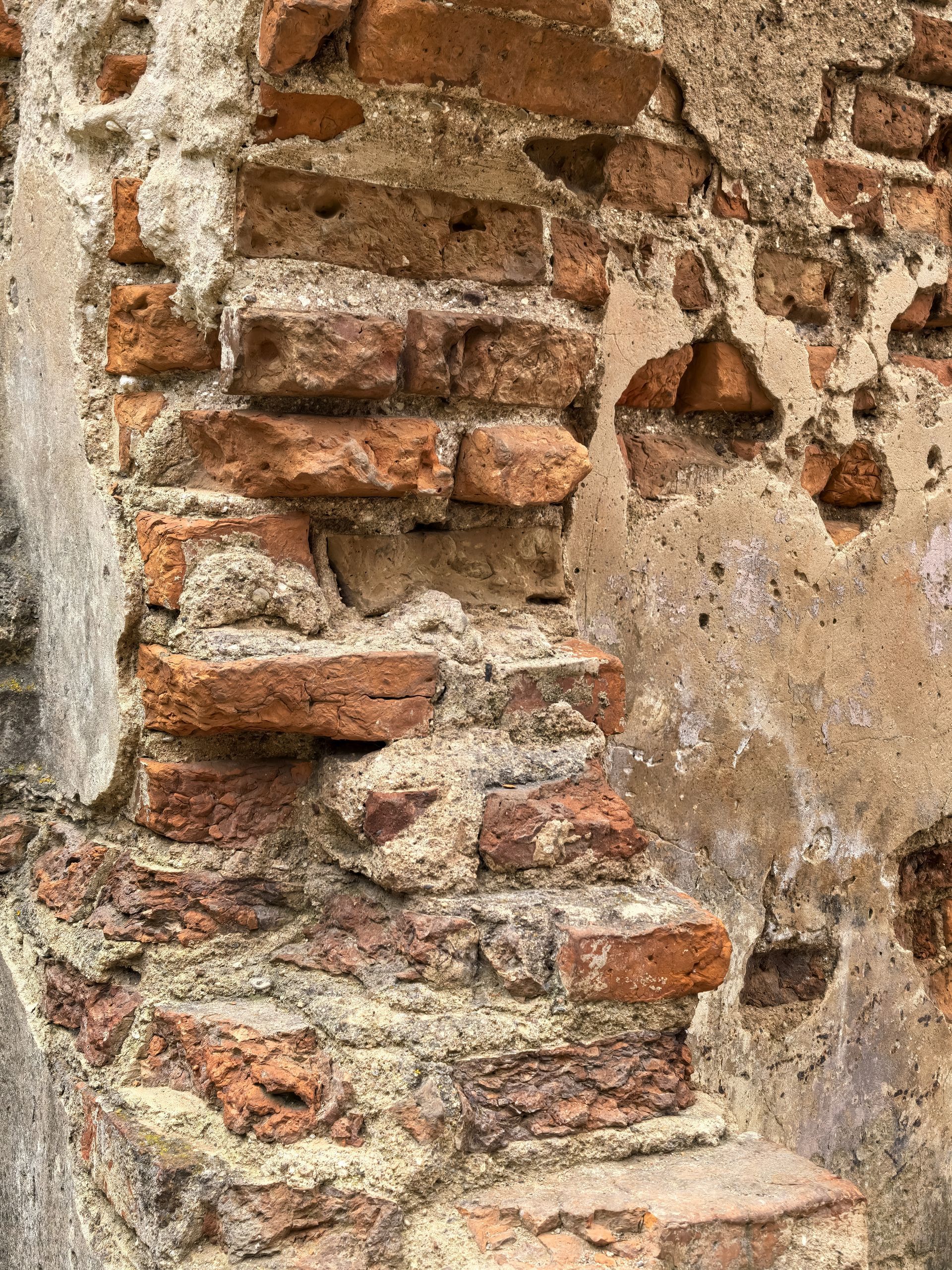 Close-up of a weathered brick wall with patches of crumbling plaster and exposed masonry. Close-up of a weathered brick wall with patches of crumbling plaster and exposed masonry.