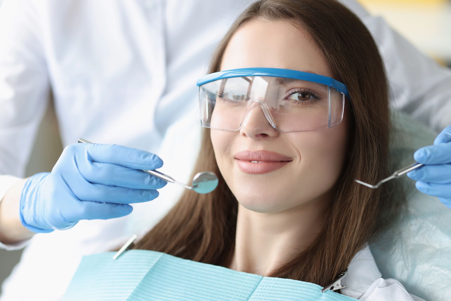Paziente odontoiatrico con visiera protettiva che sorride mentre il dentista lavora con gli strumenti in clinica.