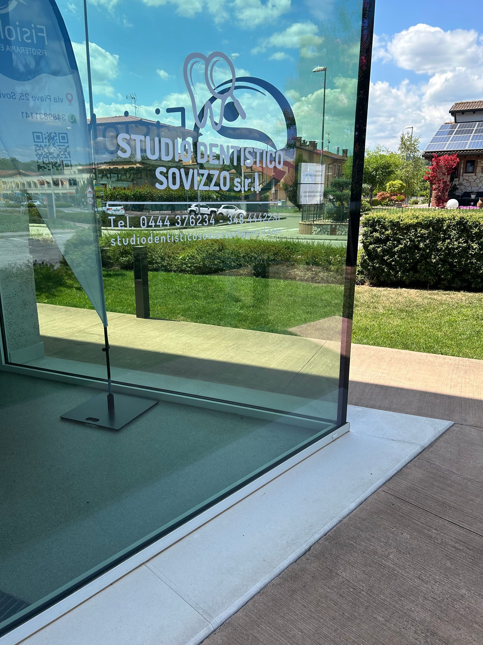 Vetrina con logo “Studio SoVez” e riflesso di una piazza esterna soleggiata