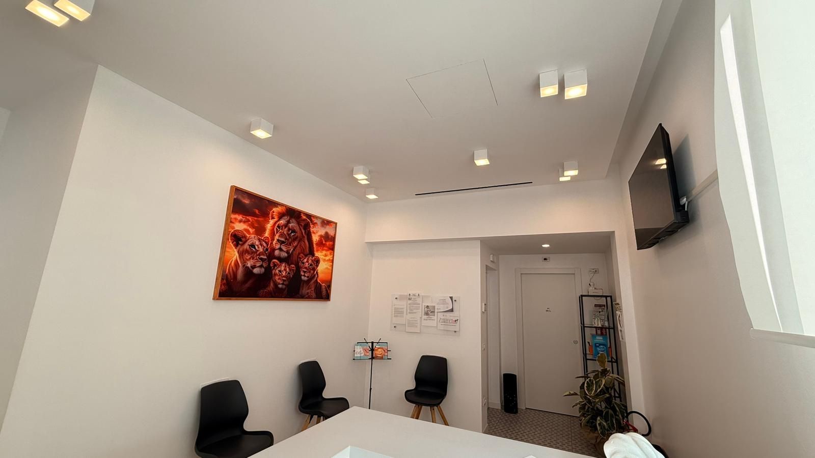Sala d'attesa minimalista per ufficio con sedie nere, pareti bianche, opere d'arte alle pareti e un televisore.