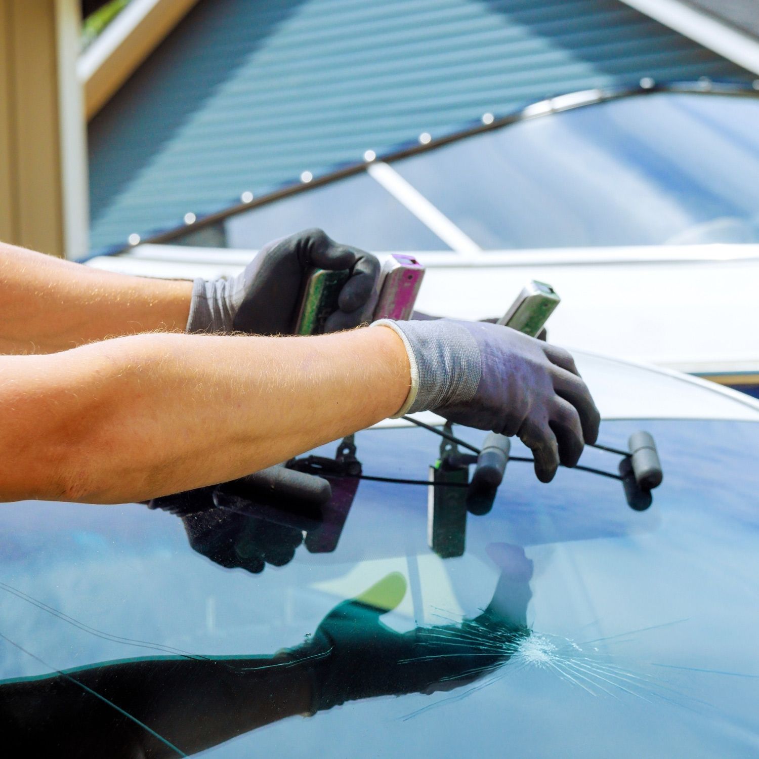 Arms in protective gloves repair a car windshield with a crack using specialized tools