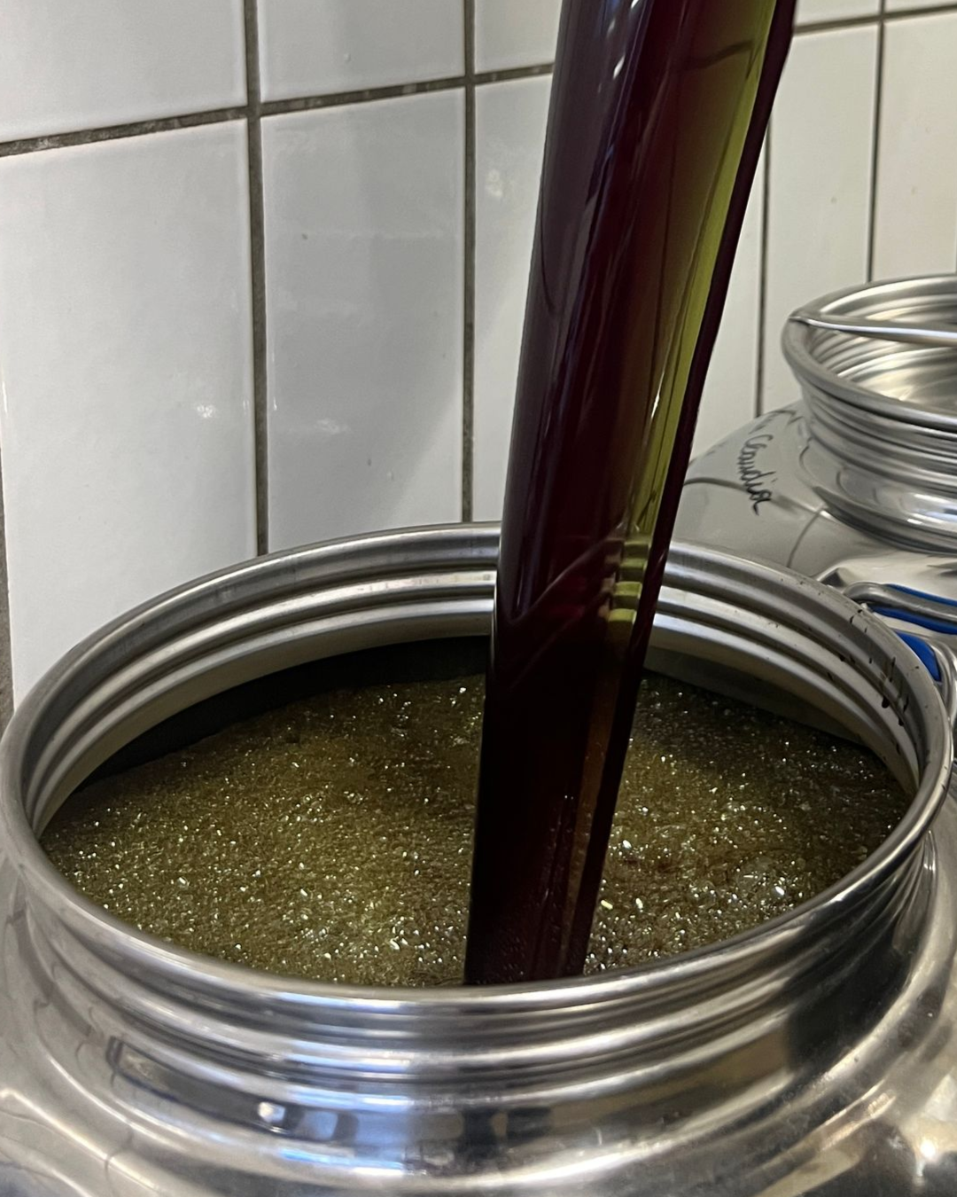 Dunkle Flüssigkeit wird in ein Metallgefäß gegossen, das mit einer grünlichen, körnigen Mischung gefüllt ist.