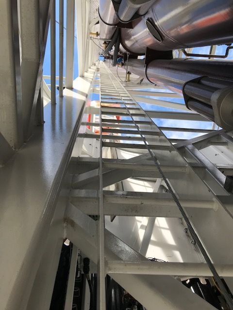 A man wearing a hard hat and safety harness is standing on top of a rocky roof. Ladder fall PROTECTION system
