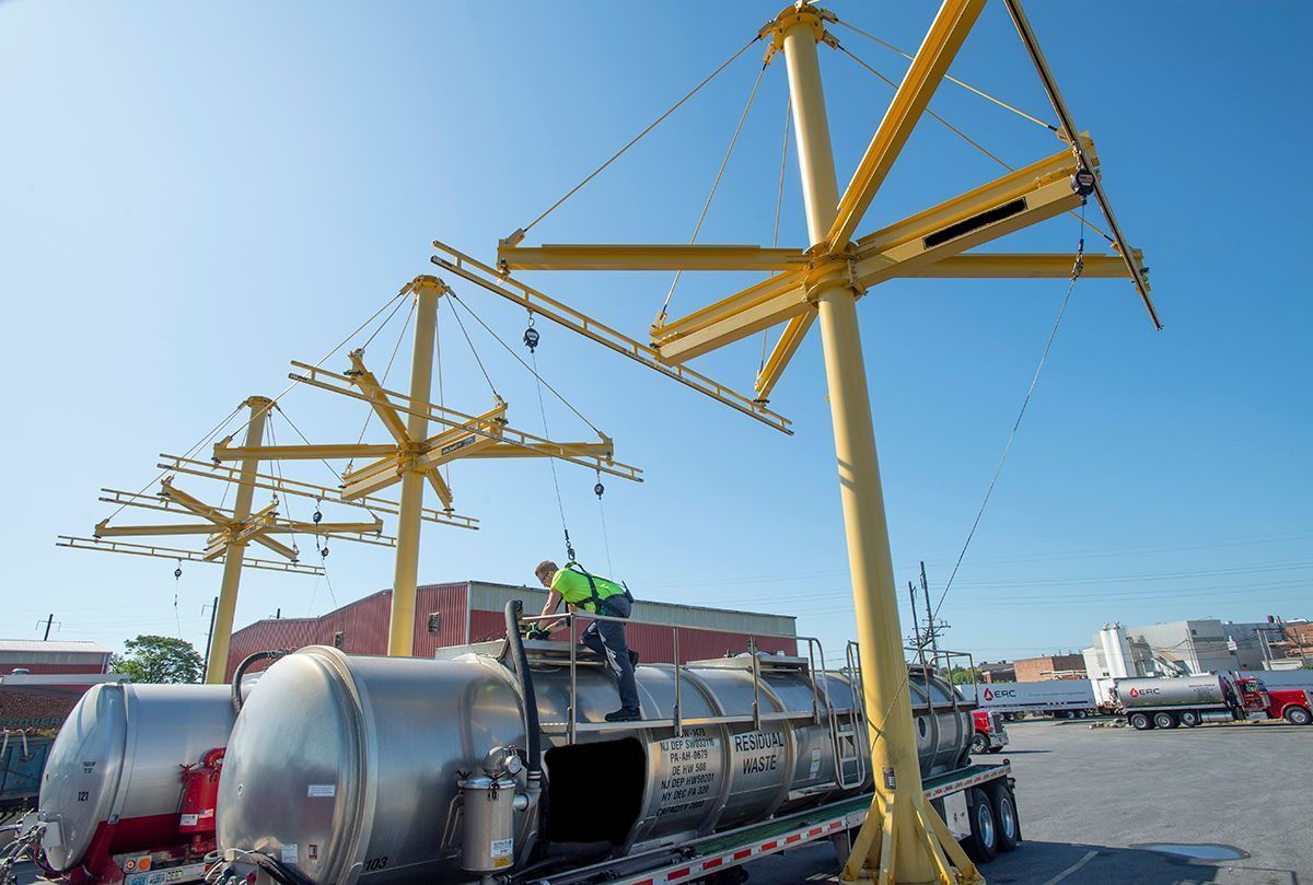 A man is standing on top of a large metal object being lifted by a crane. A man is standing on top of a large metal object being lifted by a crane.
