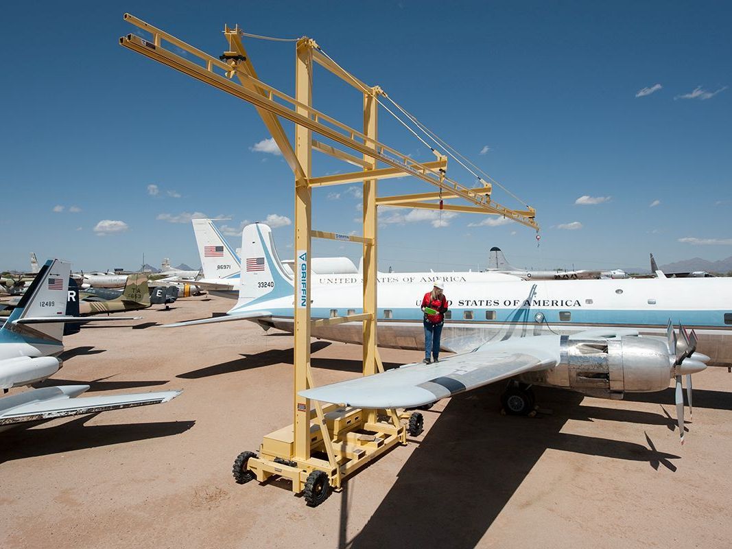A man is standing next to an airplane with a crane attached to it