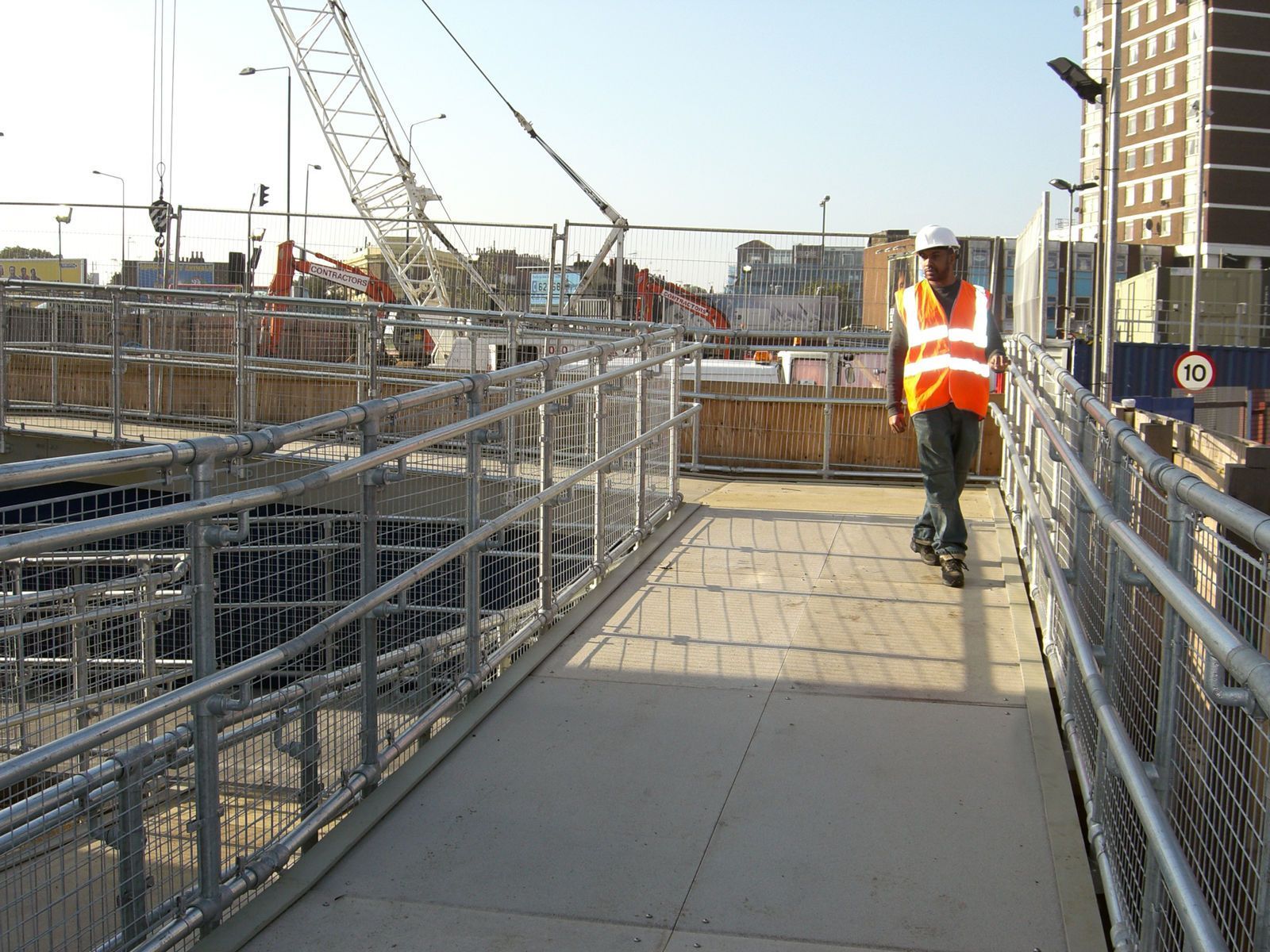 A man in an orange vest is walking across a bridge