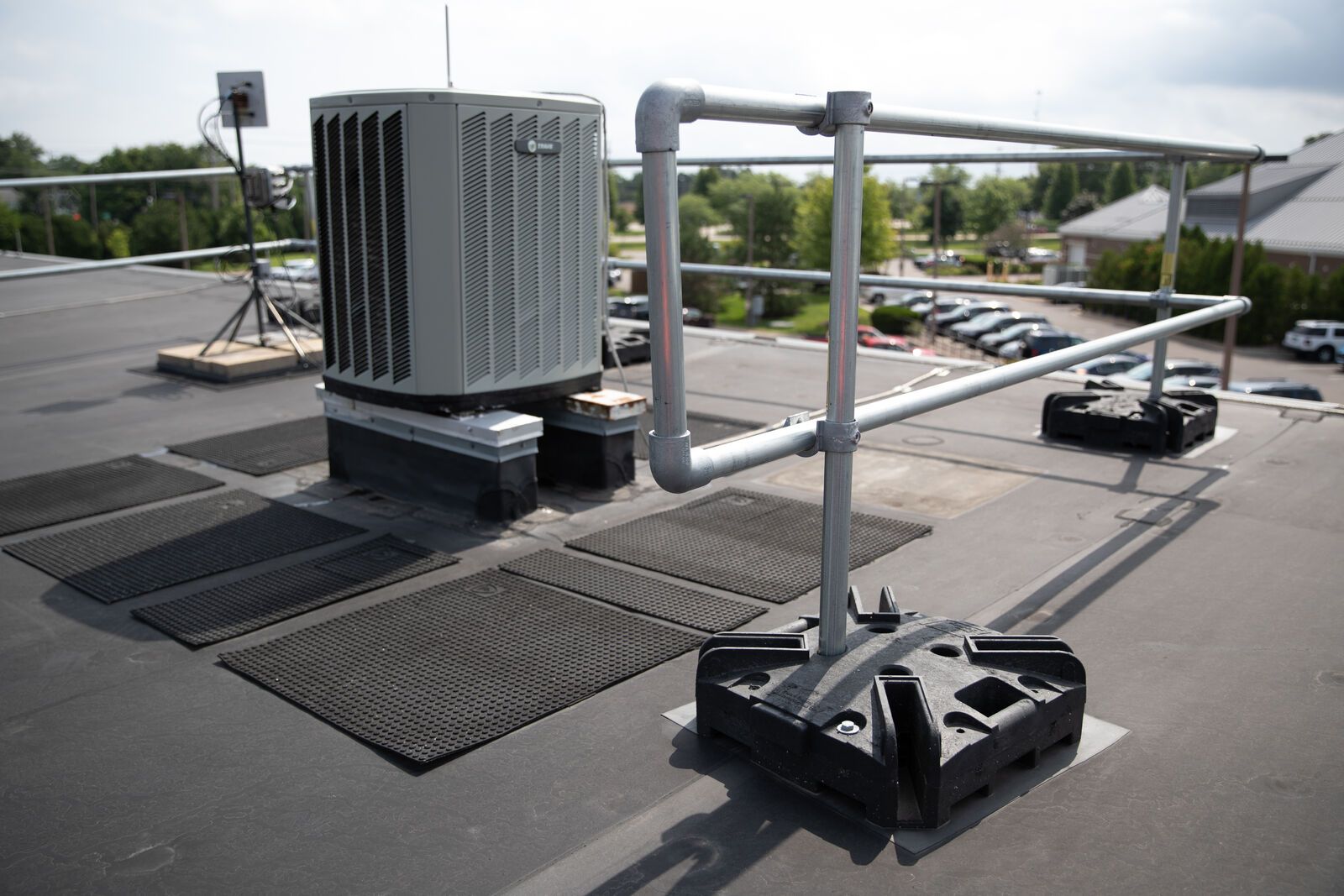 An air conditioner is sitting on top of a roof next to a railing.