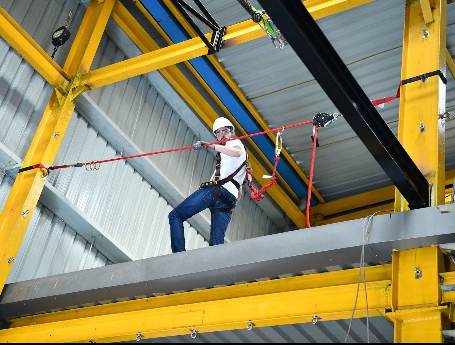 A man is standing on a beam in a building holding a rope.