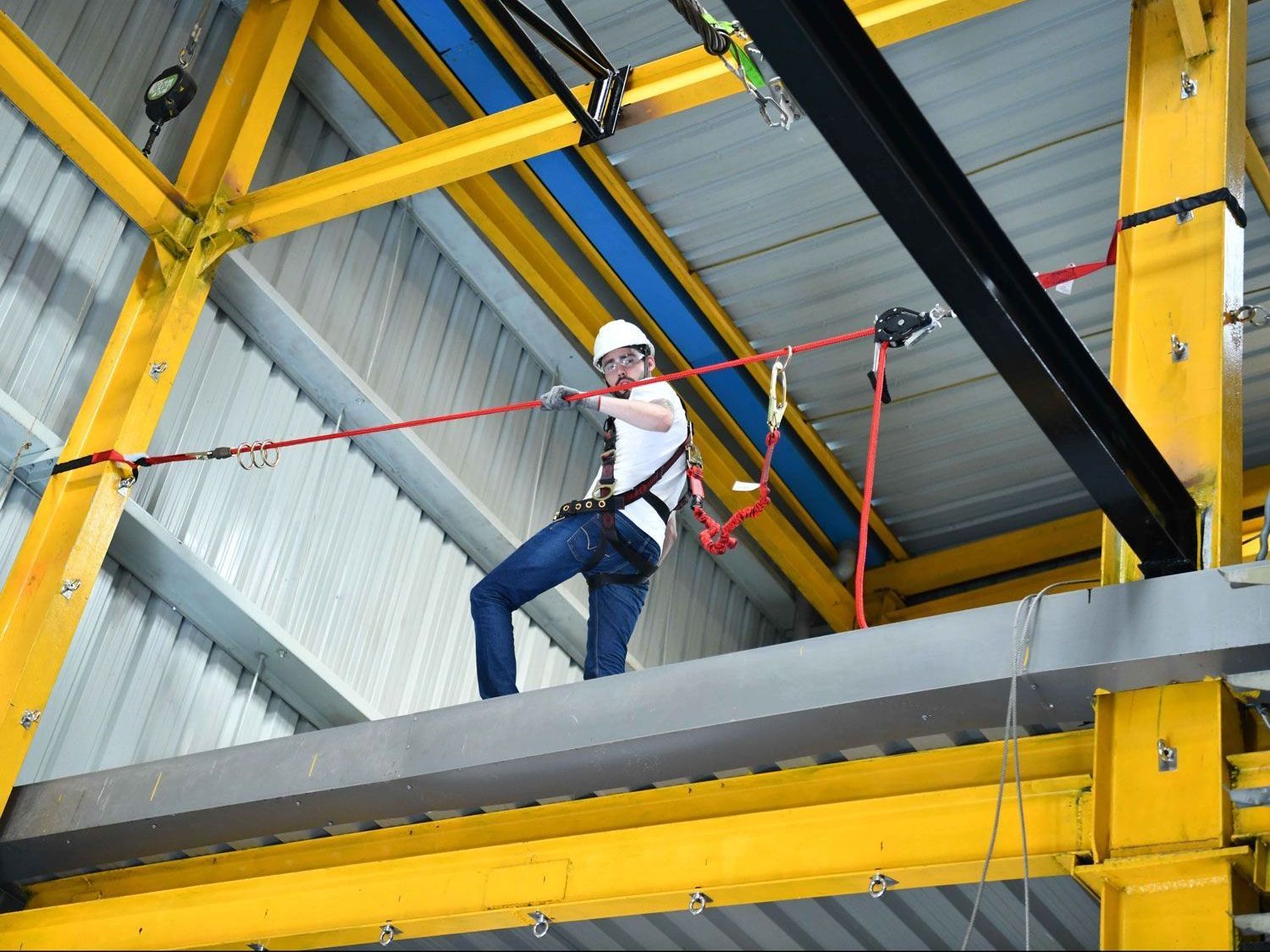 A man in a safety harness is standing on a beam in a building.