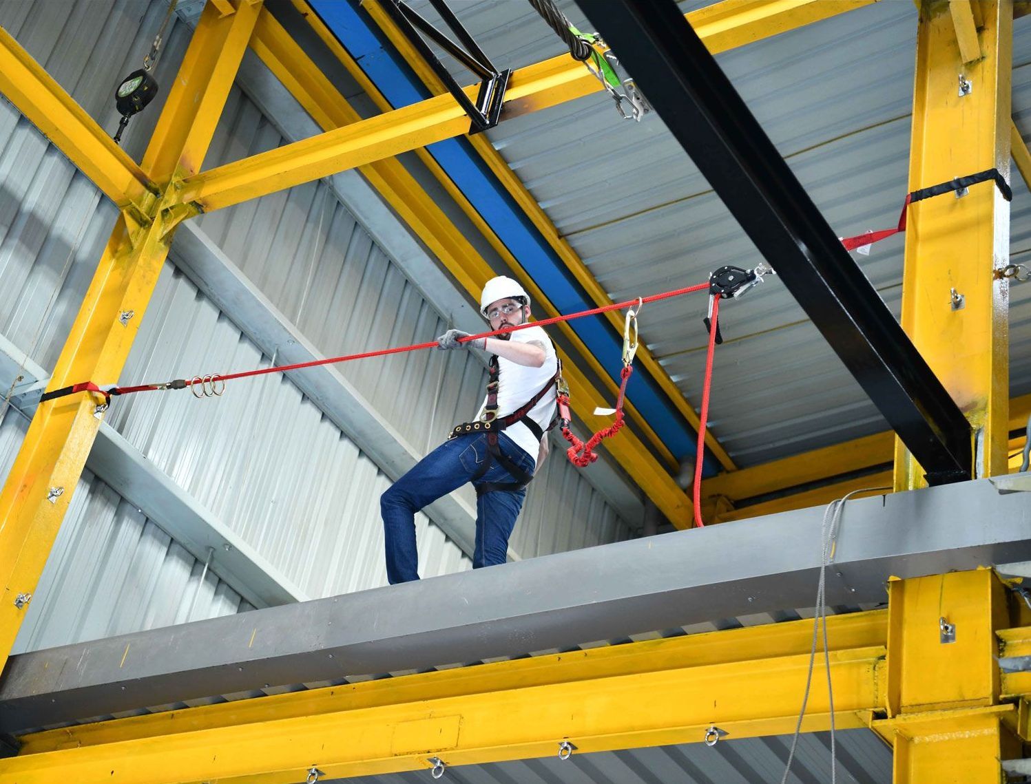 A man is standing on a beam in a building holding a rope.