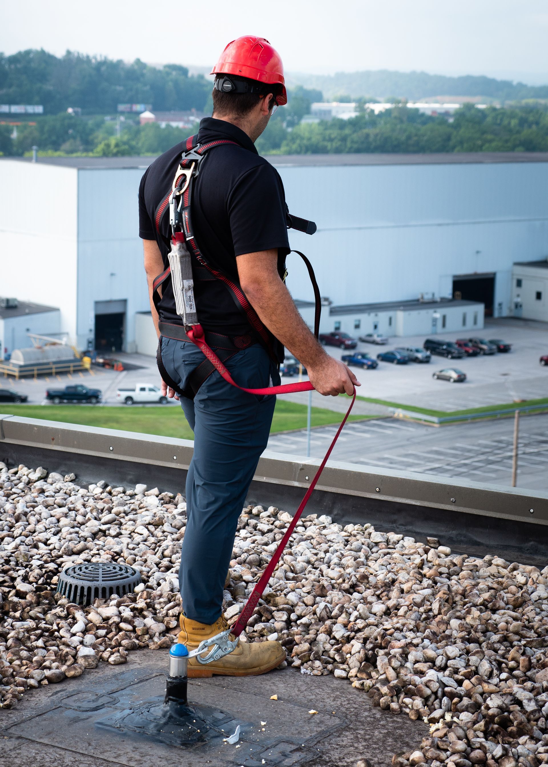 A man wearing a hard hat and safety harness is standing on top of a rocky roof. A man wearing a hard hat and safety harness is standing on top of a rocky roof.