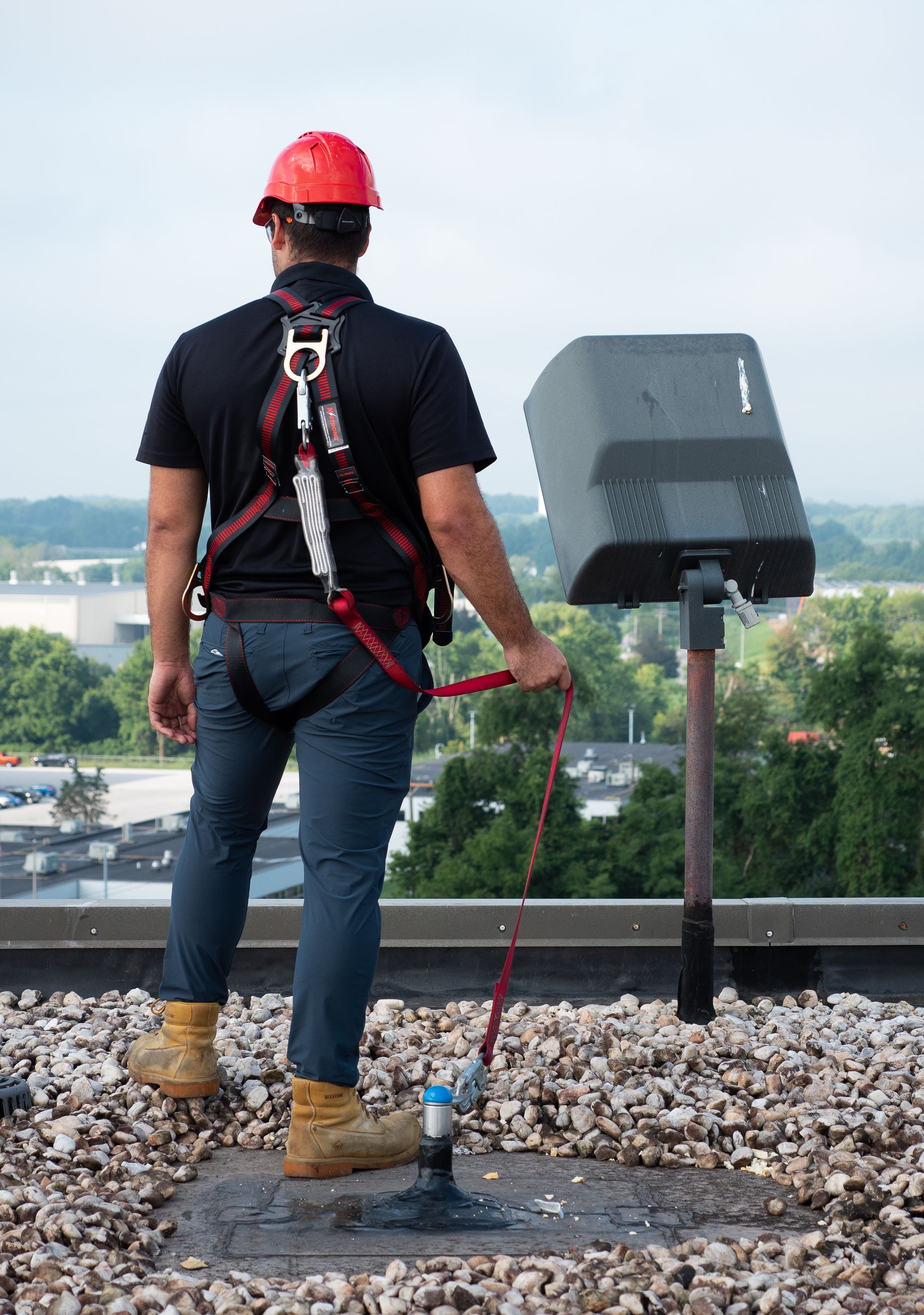 A man wearing a hard hat and safety harness is standing on a roof.