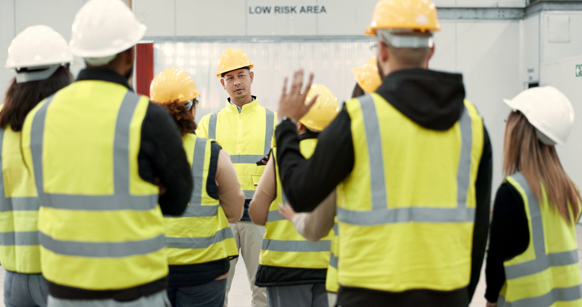 A group of construction workers wearing hard hats and safety vests are standing in a circle. A group of construction workers wearing hard hats and safety vests are standing in a circle.
