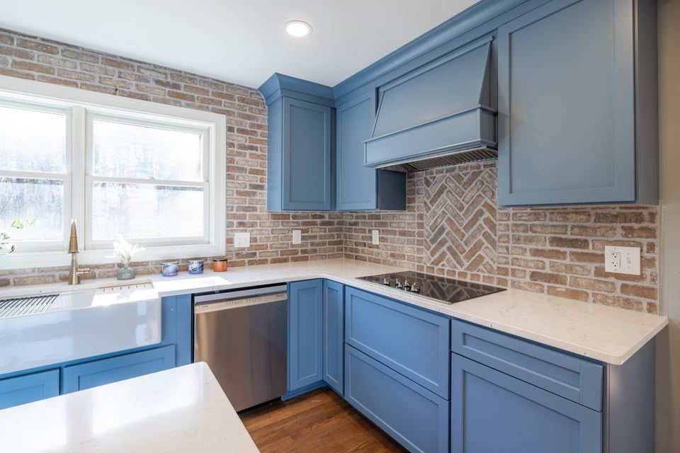 Blue and gray kitchen with brick backsplash, stainless appliances, and a window over the sink