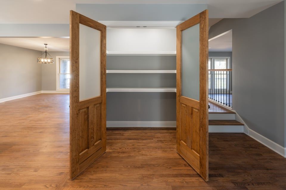 Open wooden doors framing built-in white shelves in a gray room with hardwood floors.