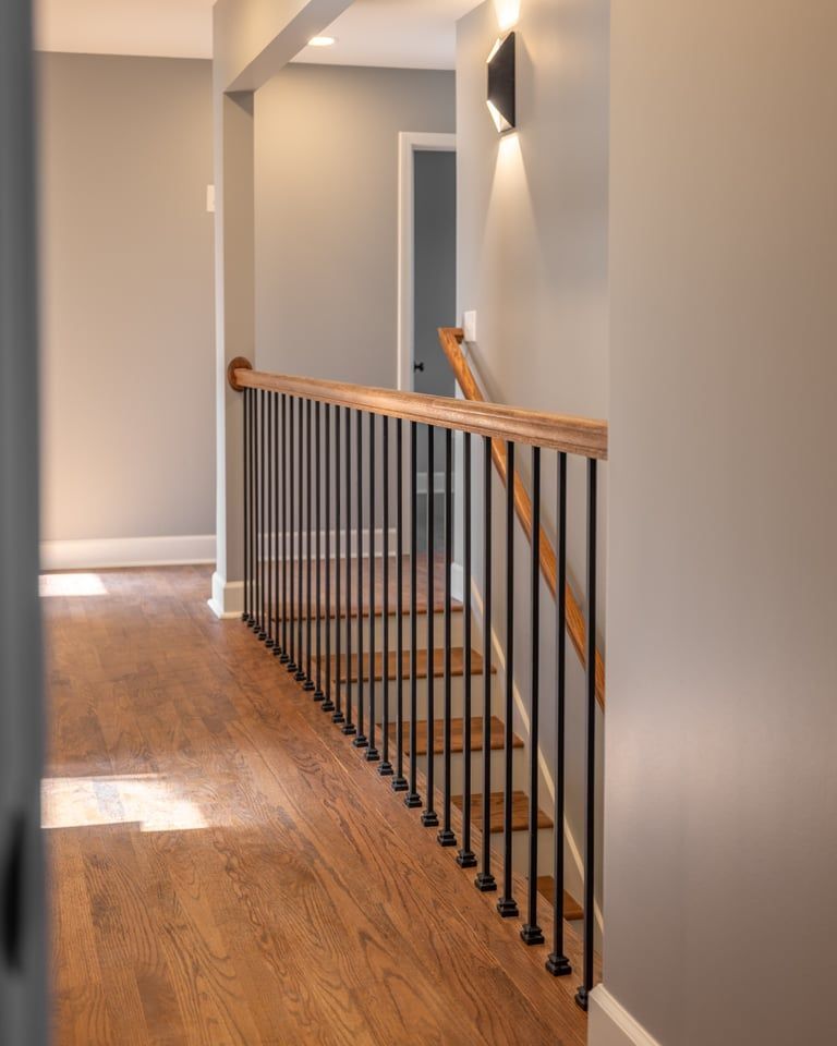 Hallway with hardwood floor and modern staircase railing, lit by sunlight
