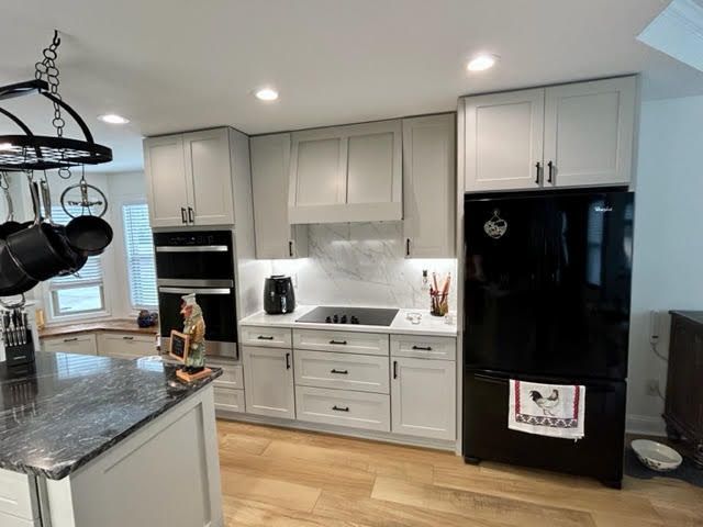 Modern kitchen with gray cabinets, black appliances, island, and wood floors