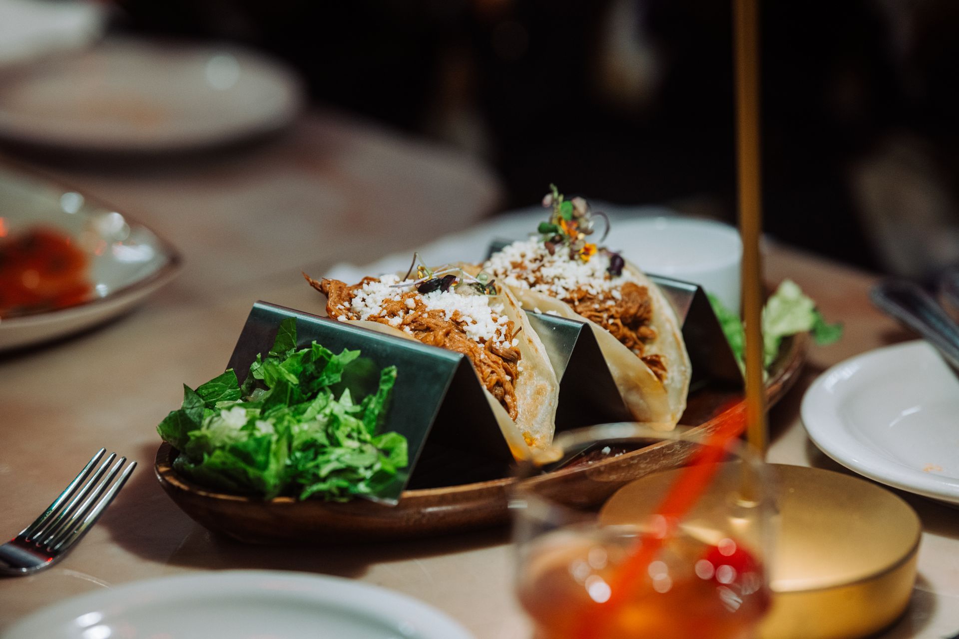 Tacos on a dark plate with greens at a softly lit dinner table