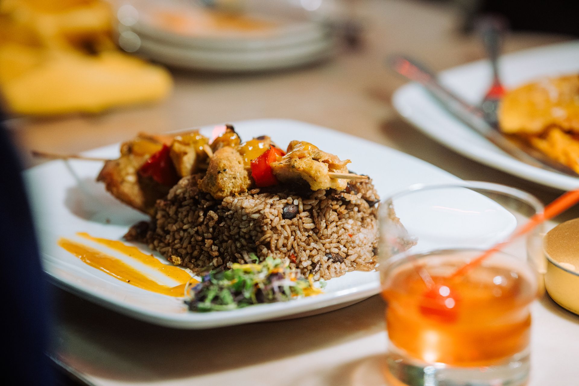Plate of rice with grilled chicken and sauce, with a drink on a restaurant table in the foreground.