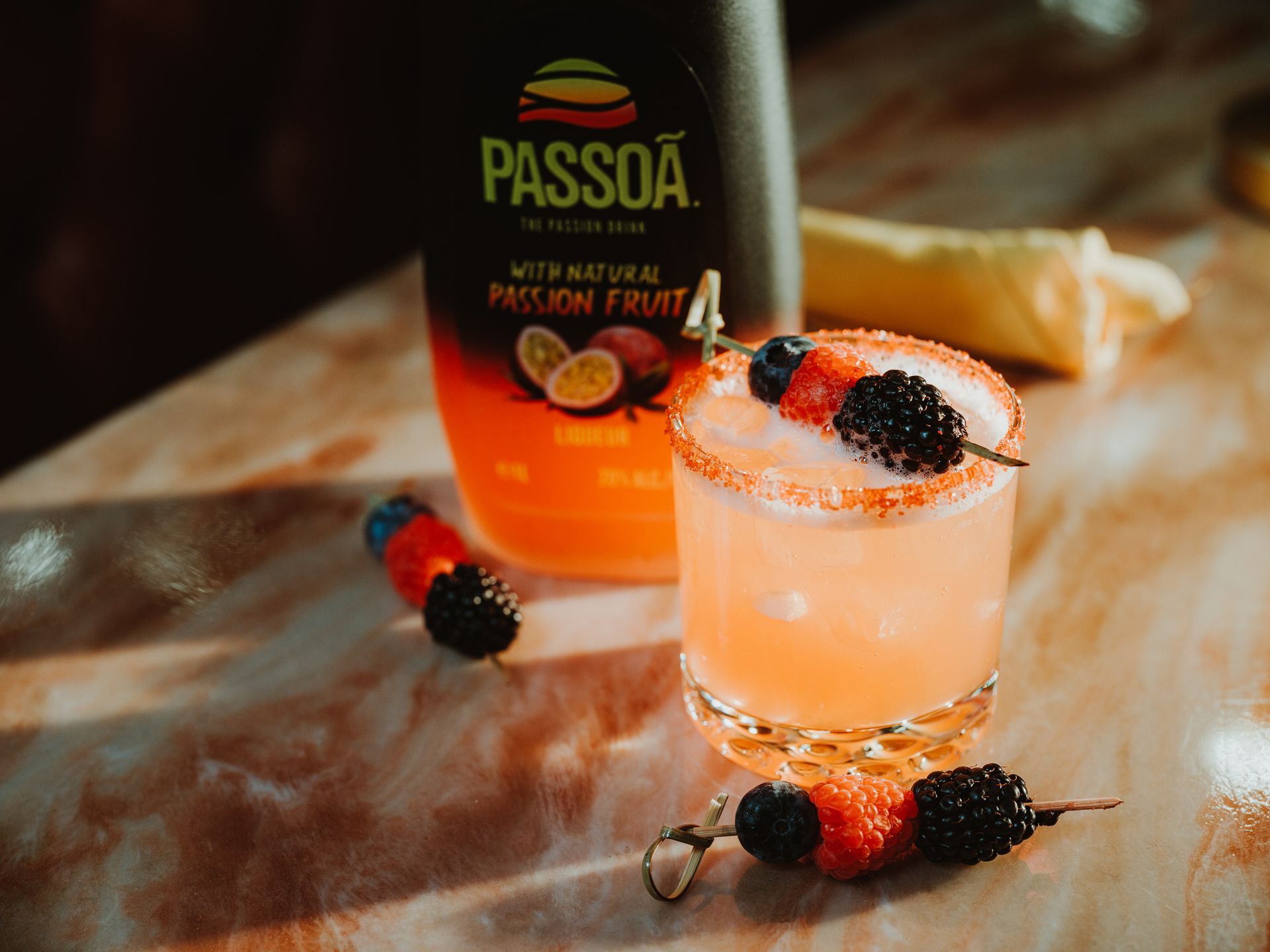 Passoã passion fruit liqueur with a pink cocktail garnished with berries and sugar rim on a marble surface
