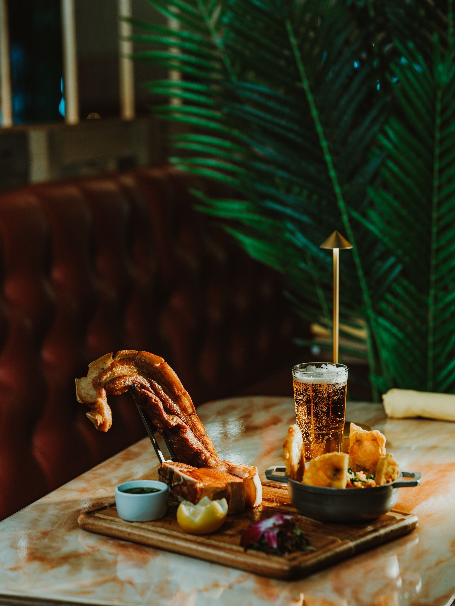 Plated gourmet meal with grilled meat, fries, and a tall cocktail on a wooden board in a dim restaurant