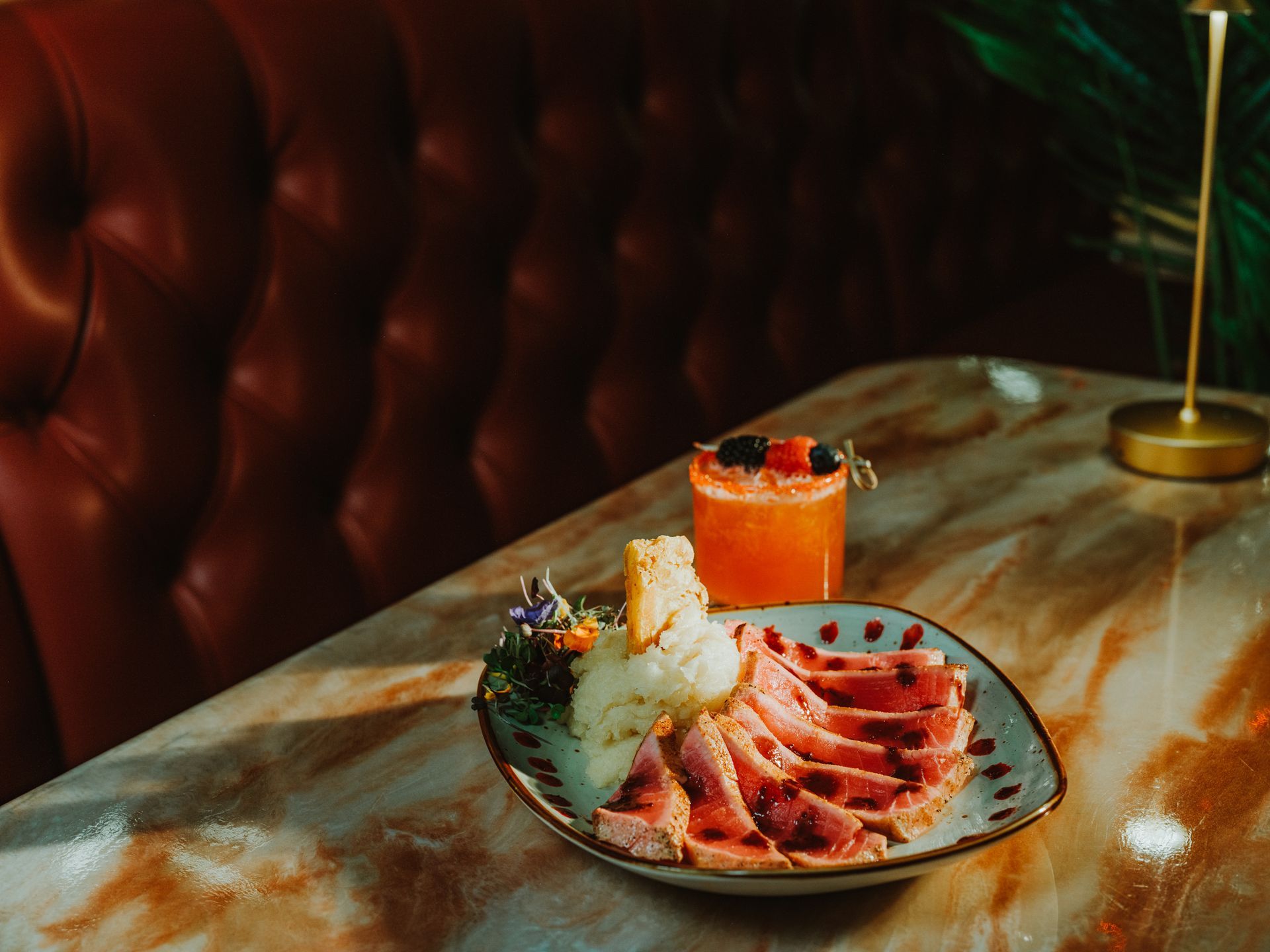 Seafood platter and orange cocktail on a marble table in a dimly lit restaurant booth