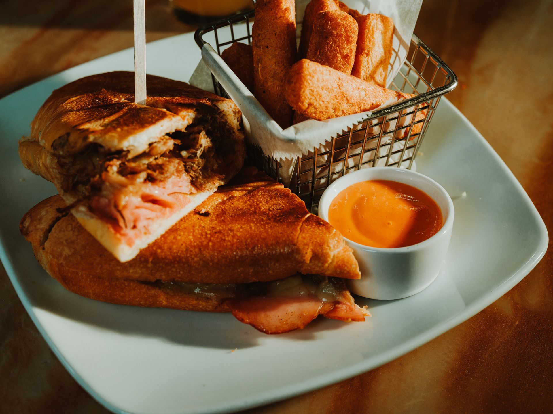Burger and fries on a white plate with a small cup of dipping sauce on a wooden table