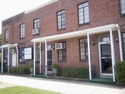 A two-story red brick building with a covered entrance, white trim, and a sign for 