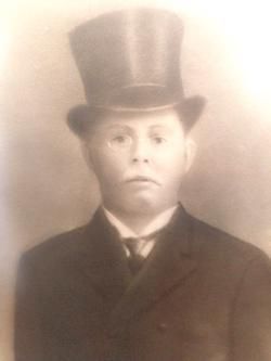 A studio portrait of a person wearing a formal suit and a top hat, captured in a sepia tone.