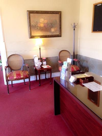 A reception area with a dark wood desk, two upholstered chairs, a small table with a lamp, and artwork on a beige wall.