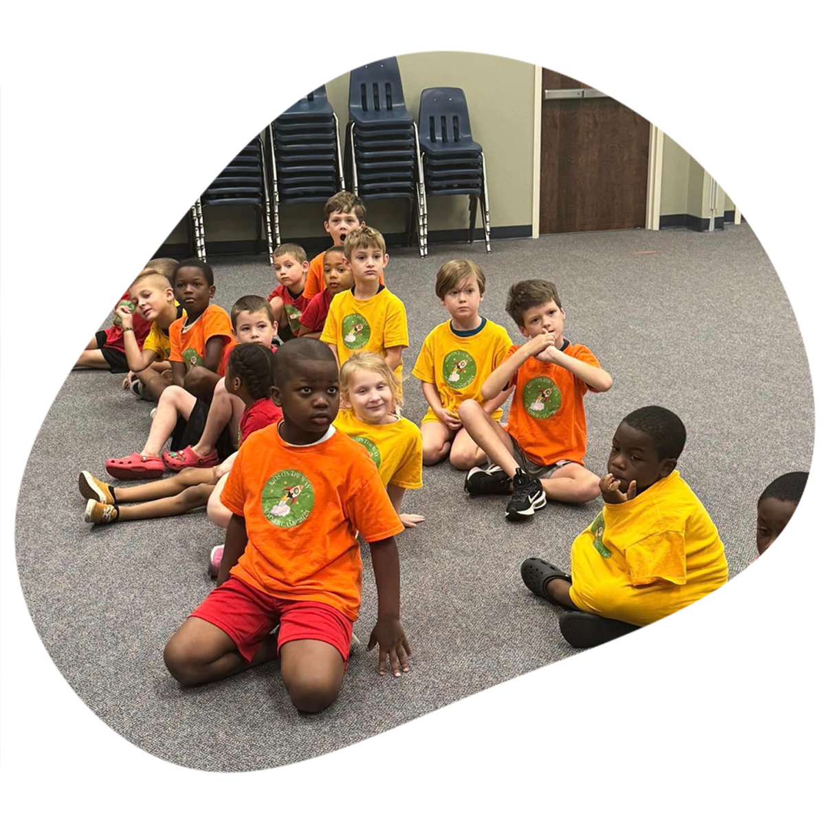 A group of children are sitting on the floor wearing orange and yellow shirts