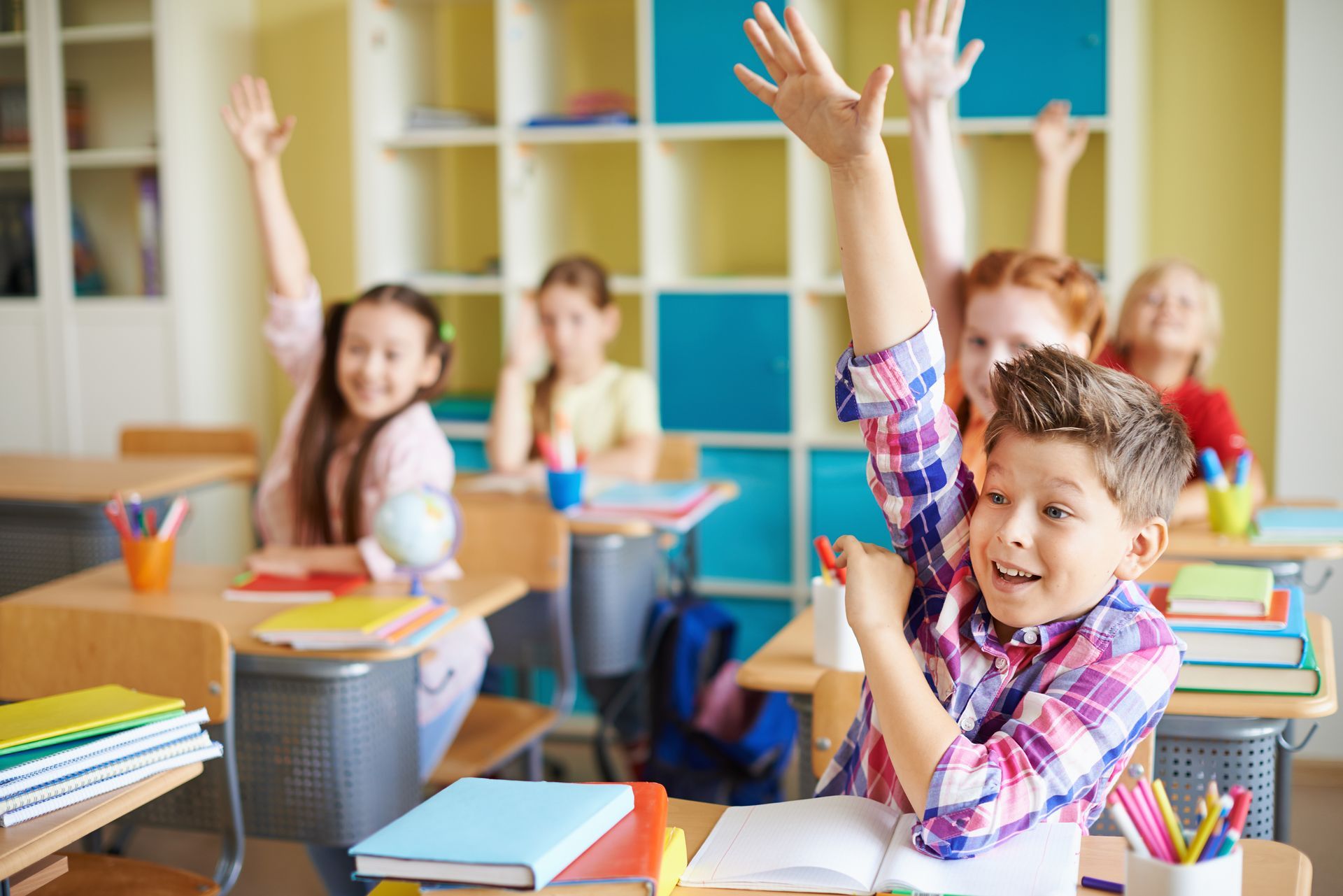 A group of children are raising their hands in a classroom.